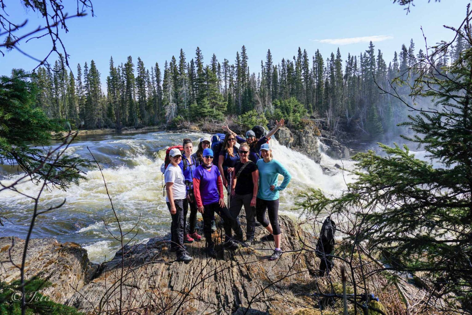 Image of a group of hikers standing on a rocky outcrop before a waterfall surrounded by forest. Practicing safety while recreating and hiking in groups lends to sustainability as well.