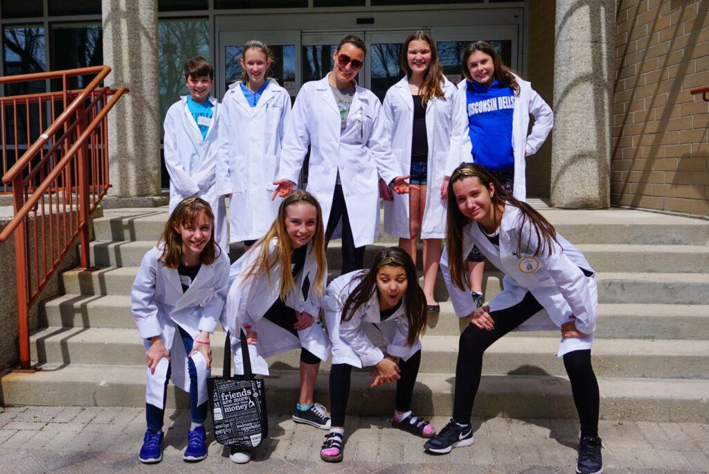 A group of students with their teacher  wearing lab coats standing on the steps of a building. Teaching kids about sustainability is crucial for maintaining sustainable development.