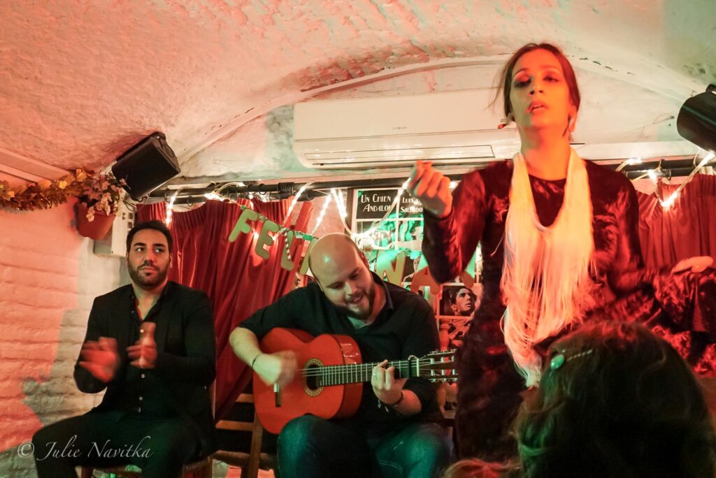 Image of a dancer with guitarist in a low-lit small tavern-like flamenco club in Granada, Spain. Supporting the arts while on a city trip can make your visit more sustainable.