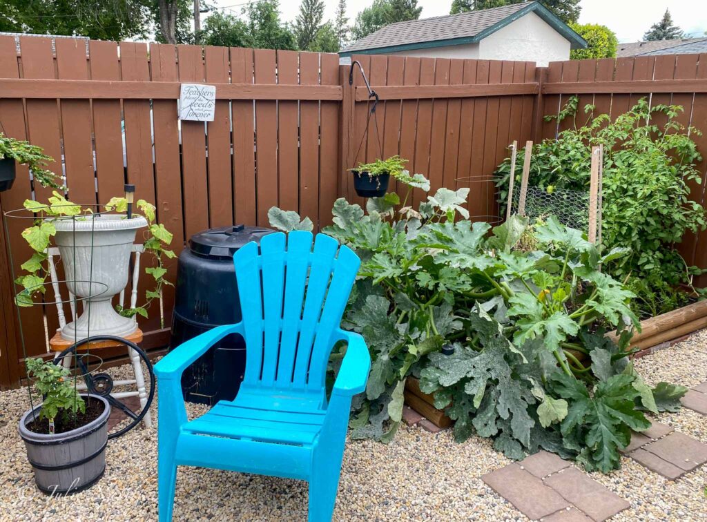 Image of small vegetable garden next to a compost receptacle, patio chair and potted plants. Growing a garden and composting can lead to a more sustainable house.
