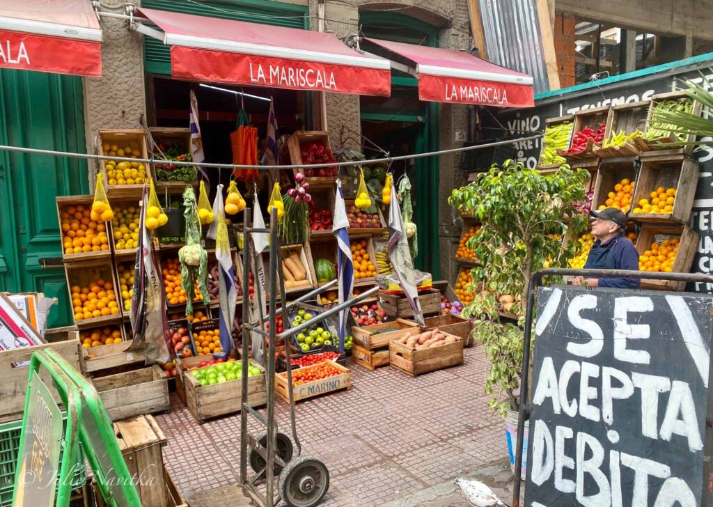 Image of a storefront with a variety of local produce set up for sale on the sidewalk. Buying local and in-season food is one way to travel more sustainably. 