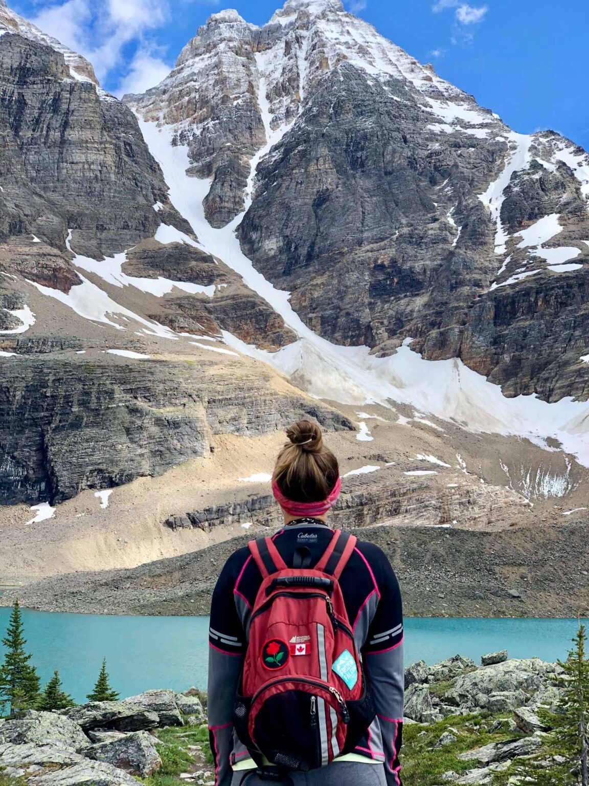 Picture of hiker photographed from behind looking out over a landscape of towering mountains and turquoise lake. The power of your own two feet is the most sustainable way to recreate.