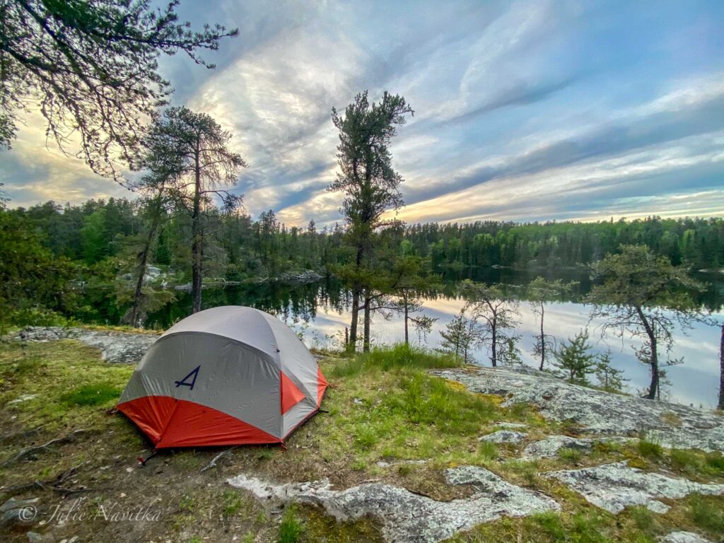Image of a tent set up overlooking a lake surrounded by trees nearing dusk. Sustainable recreation and eco-friendly camping means being careful to practice the seven principles of Leave No Trace.