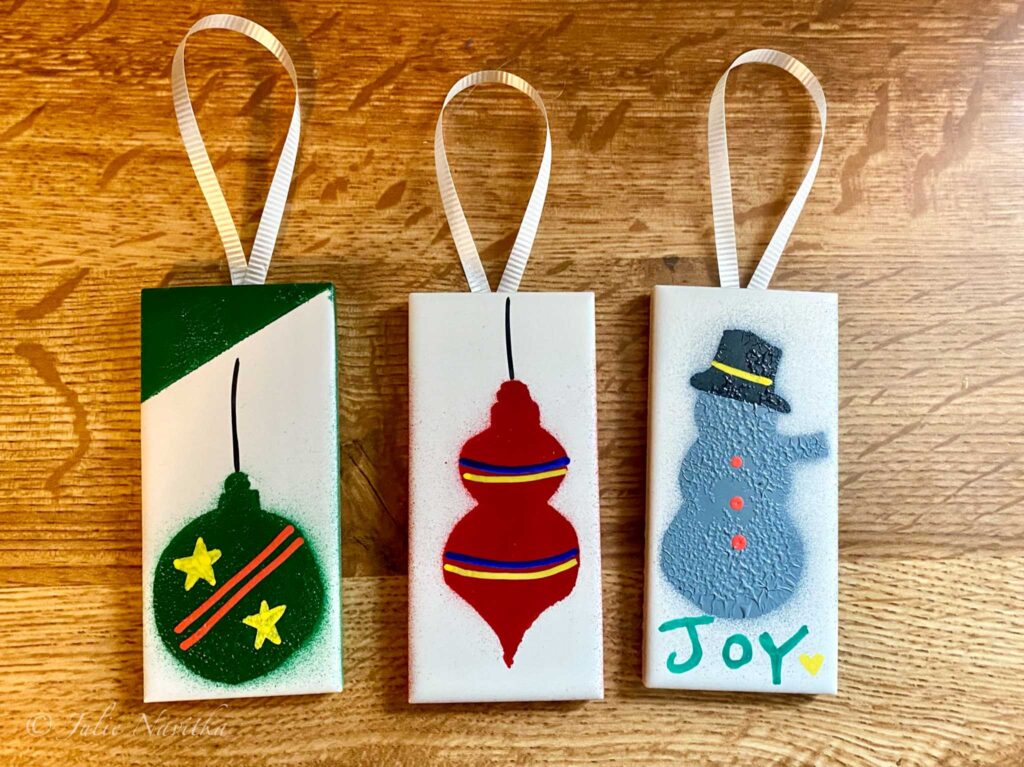 Image of three holiday ornaments made from up-cycled kitchen tiles and gift ribbon. Re-using materials and items rather than throwing them in the garbage promotes sustainability and up-cycling projects are a fun way to teach children about sustainability.