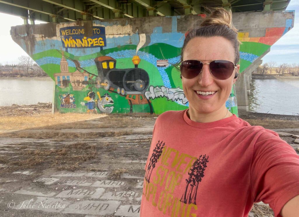 Image of a runner stopped under an overpass with a mural painted in the background reading "Welcome to Winnipeg".