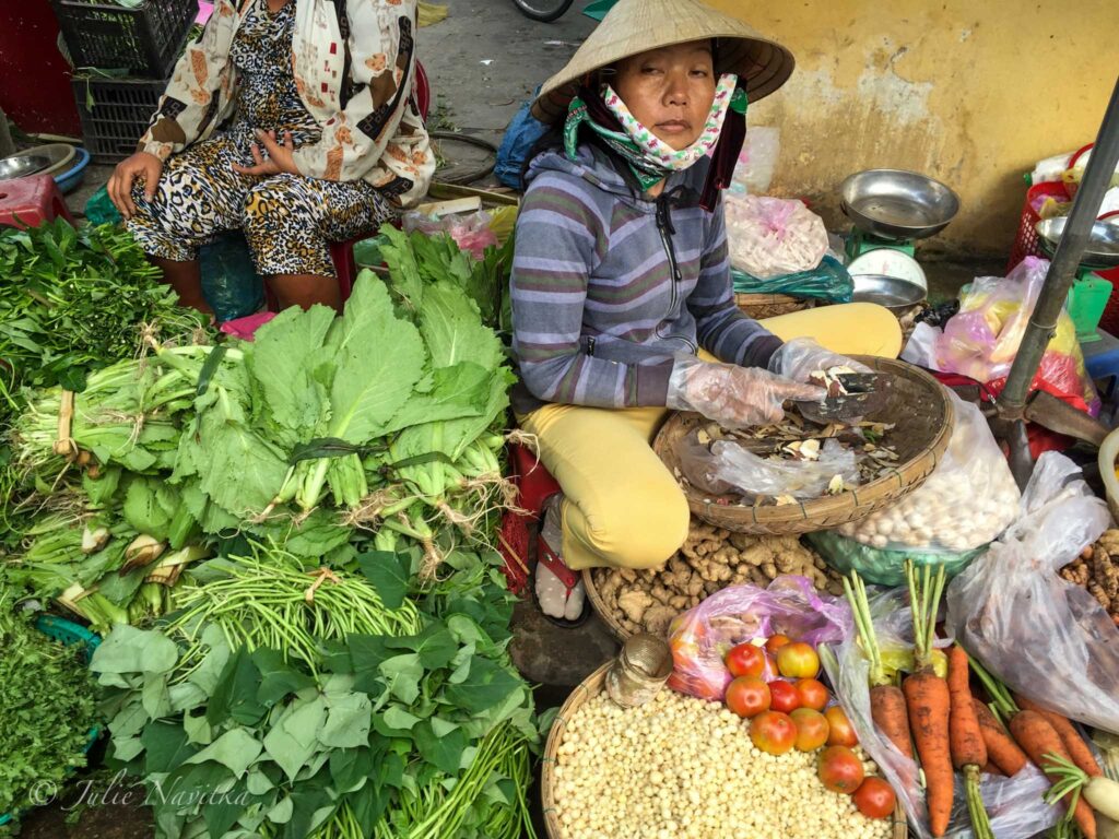 Image of vendor amongst their vegetables in a market in Hoi An, Vietnam.