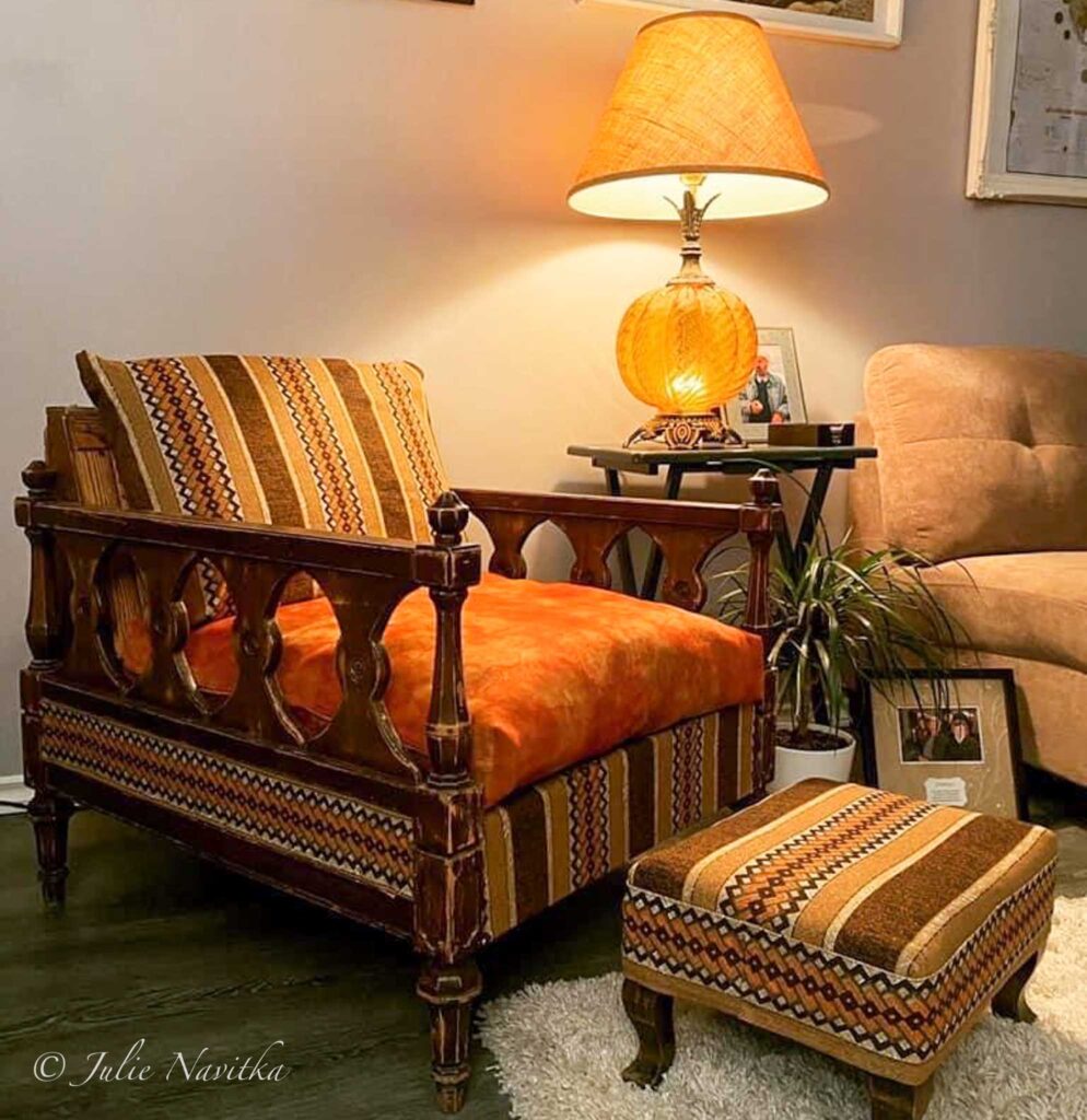 Image of a retro-style chair with footstool (re)covered in orange and brown patterned fabric. Purchasing second-hand furniture is a sustainable way to furnish your home.