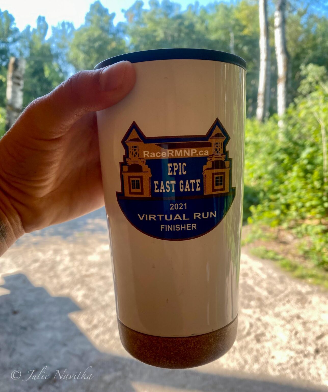Up-close image of travel coffee mug with forested background. Re-usable beverage containers are a must when it comes to recreating sustainably.