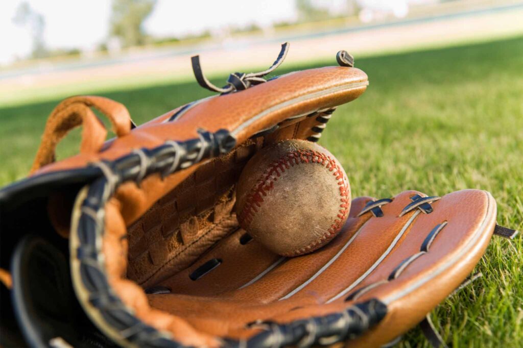 Image of a baseball glove lying on the grass with a baseball tucked inside. Purchasing second-hand sports gear lends to a more sustainable lifestyle and eco-child's play.