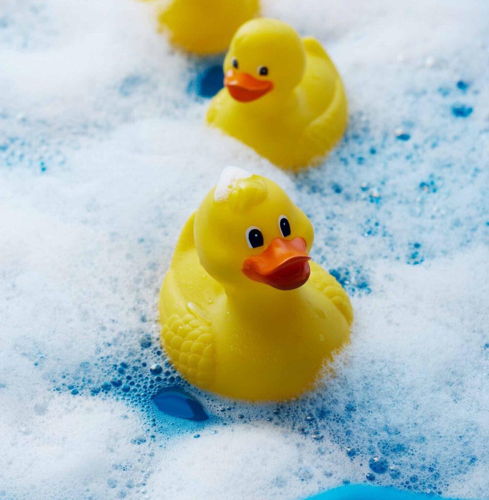 Image of rubber duckies floating in blue water with foam. Rubber isn't considered a very sustainable material.