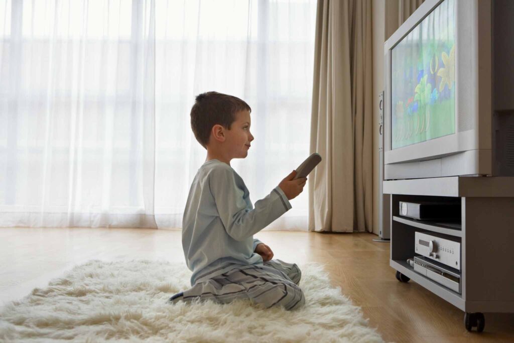 Image of a child sitting close to a TV holding a remote. 