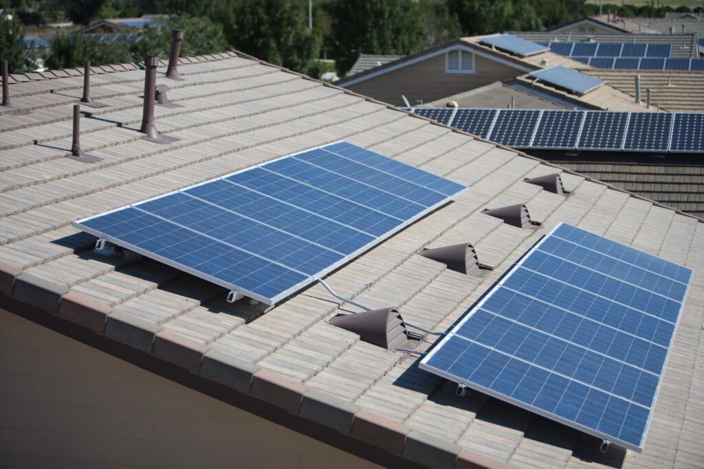 Image of the roof of a house with two solar panels on top, Other roofs can be seen in the background, also with solar panels. Converting to solar polar can lead to a more sustainable home.