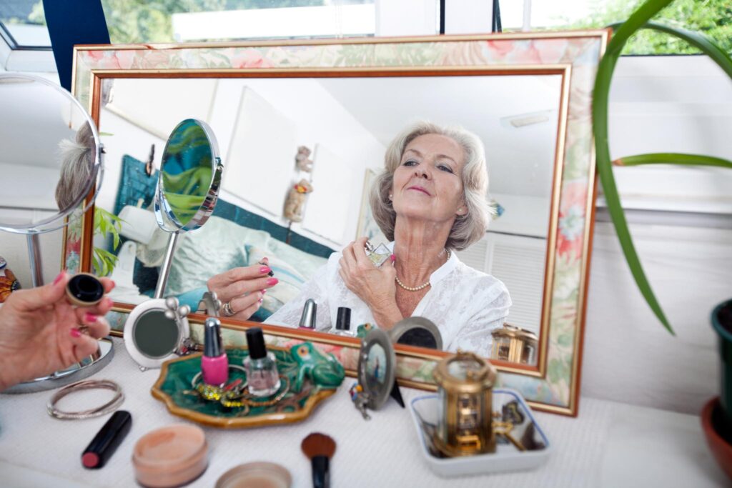 Image of a woman reflected in a mirror applying cosmetics, with an array of makeup and tools on the surface in front of her. Opting for refillable and eco-friendly packaging for beauty products is a sustainable lifestyle choice.