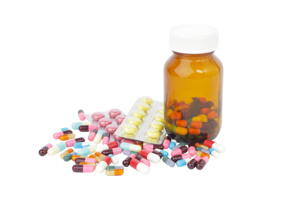 Image of a glass pill bottle with a variety of pills scattered at its base. Proper disposal of medication is essential for a sustainable lifestyle.