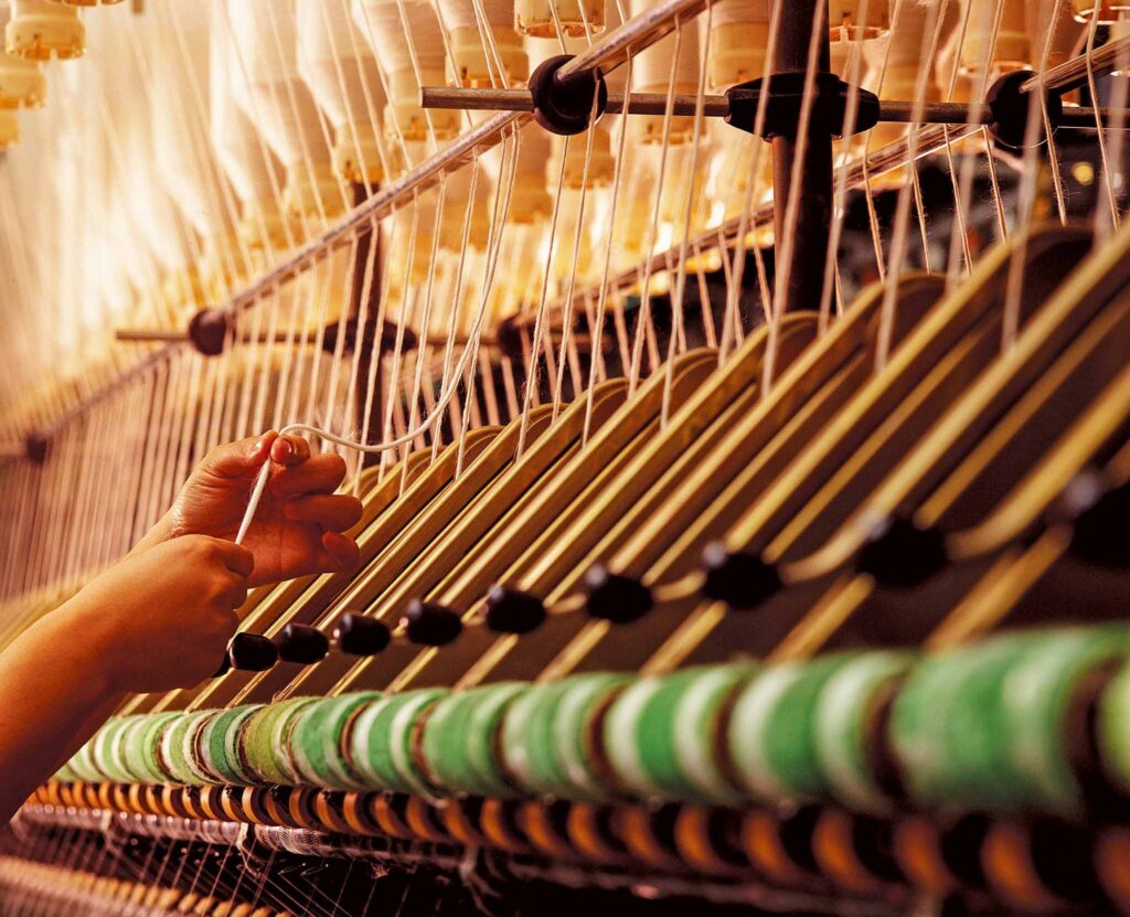 Image of hands operating a weaving loom. Social sustainability encompasses ethical manufacturing.