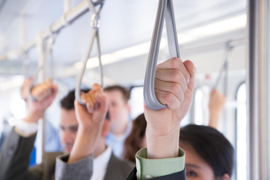 Image of several hands holding the overhead straps on a subway. Taking public transport to work helps you lead a more sustainable lifestyle.