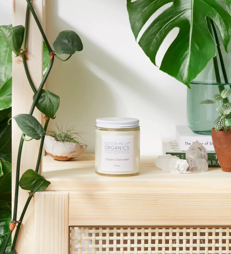 Image of the Natural Organic Sunscreen by Butter Me Up Organics on a table surrounded by plants. Non-toxic skincare is essential for a clean beauty routine. 