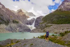 Image of a lone hiker wearing a backpack looking at a mountain lake and scenery with glacier.