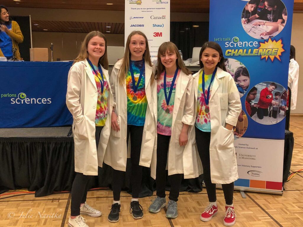 Image of four young students in lab coats posing for a picture with their winning medals for a Science competition.