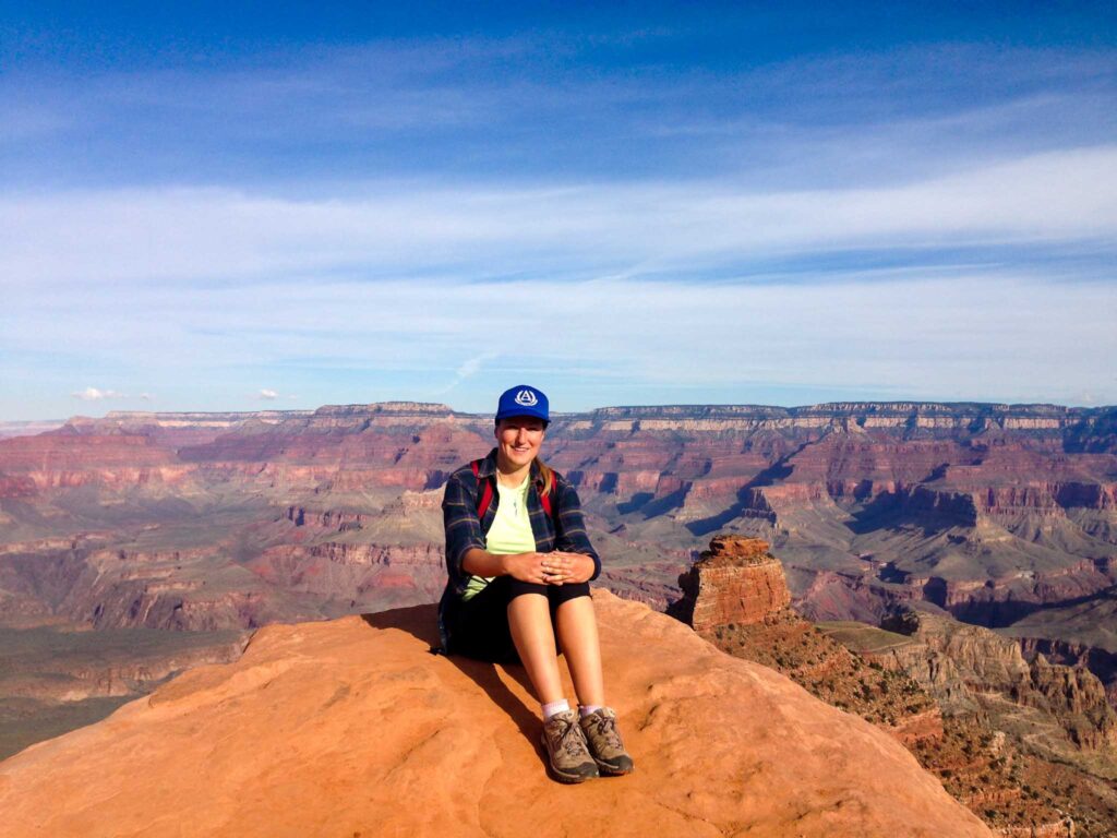 Image of a smiling hiker sitting on a ledge overlooking the Grand Canyon in Arizona. The Leave No Trace Principles are an important aspect of sustainable recreation.