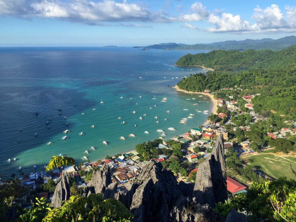 View from above of a small beach town including turquoise waters, small boats, adn lush greenery. 