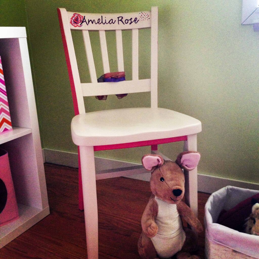 Image of a wooden chair painted pink with the name "Amelia Rose" scripted across the backrest. Crafting and upcycling is a sustainable way to create unique pieces for children.