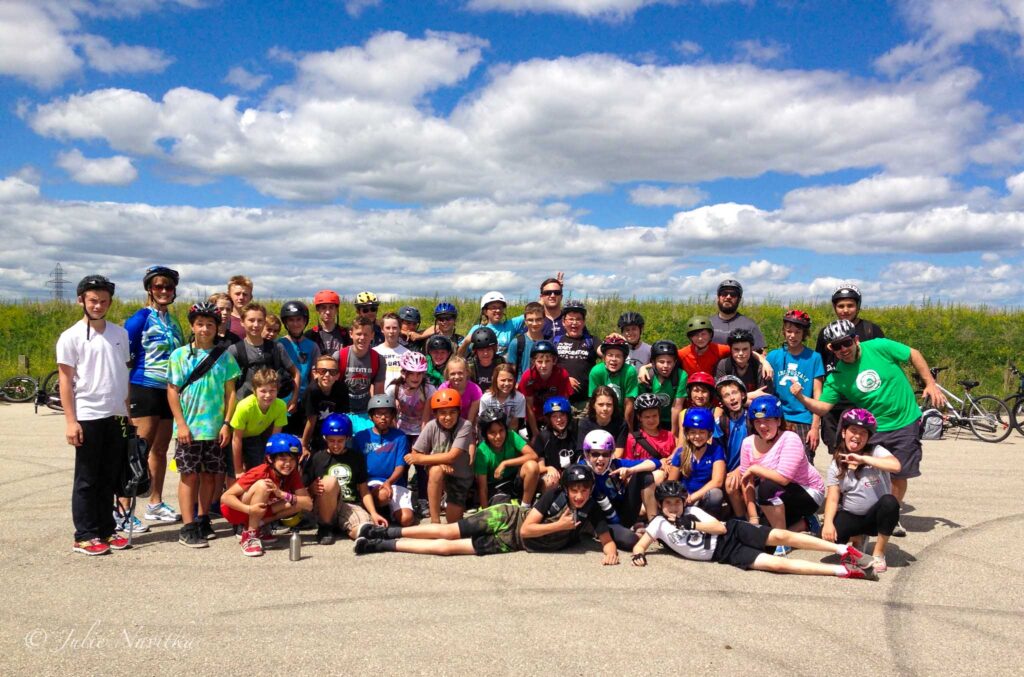 A large group photo of people, adults and teens, wearing bicycle helmets with blue sky in background. Teaching kids to appreciate the outdoors and encouraging cycling to school can make schools more sustainable.