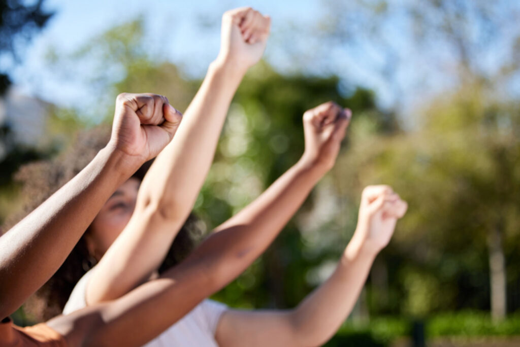 Image of four arms raised in fists seemingly in protest or support with blurred background. Youth are often some of our most passionate human rights advocates.
