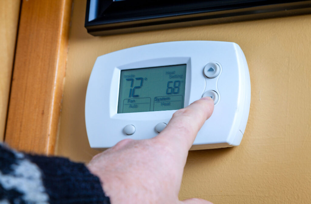 Image of a hand adjusting a digital thermostat showing 72 degrees. Adjusting the heating and cooling in schools by just a couple of degrees can make a big difference in energy consumption and costs. 