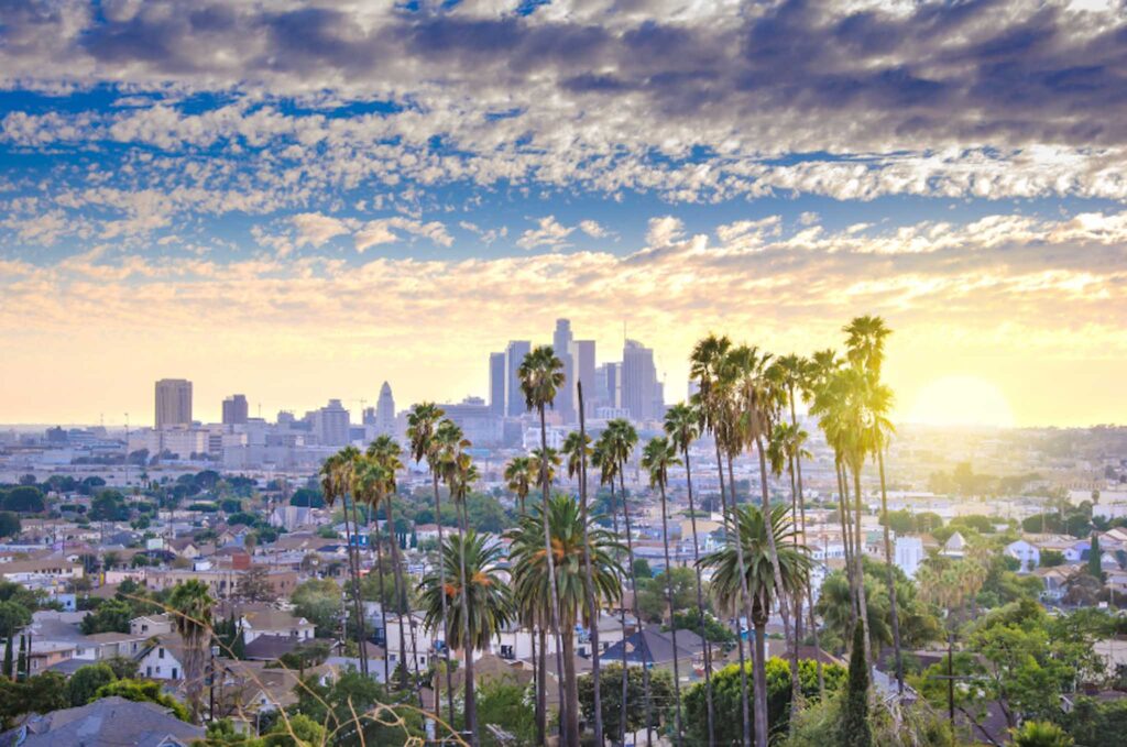 Image of the LA skyline nearing sunset with palm trees in foreground. Los Angeles is ranked 14 out of 100 on the The Arcadis Sustainable Cities Index 2022.

