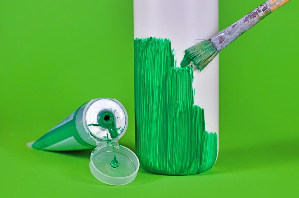 Image of a plastic cosmetics bottle being painted green. Beware of greenwashing when purchasing products for a sustainable lifestyle.
