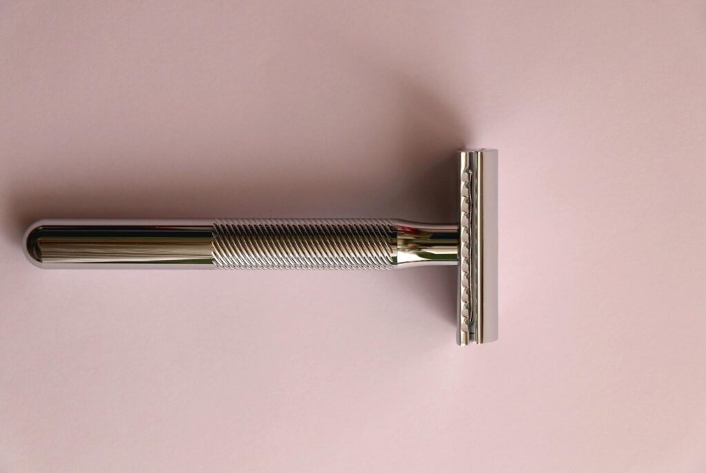 Image of a metal razor against a clean pastel pink background. Metal is a more sustainable choice than disposable plastic razors.