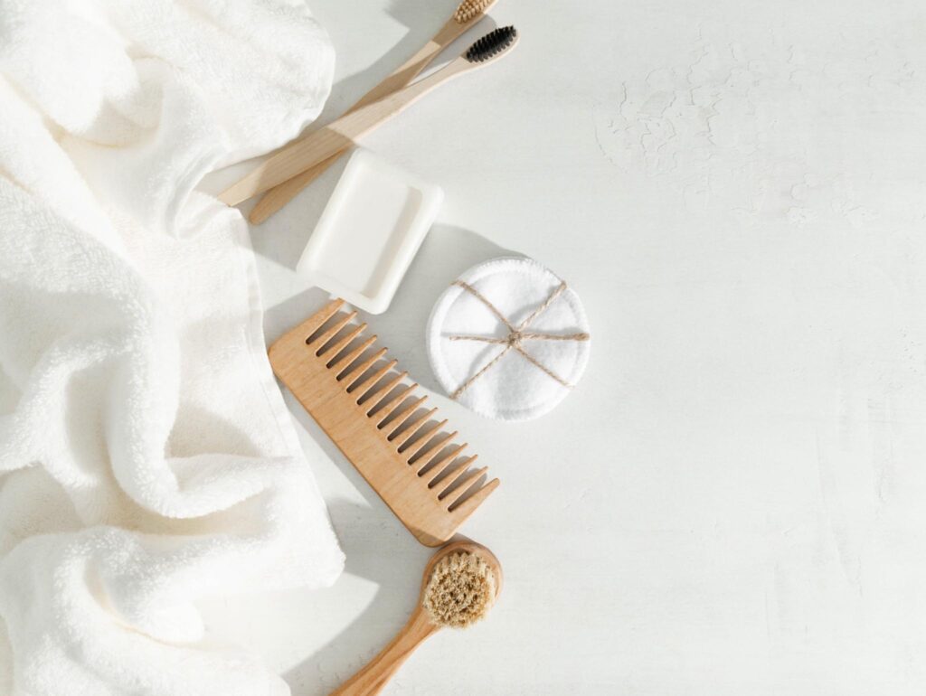 Image of wooden bathroom accessories with white cotton towels and washcloth. Sustainable materials like bamboo and organic cotton are a good choice for your health and beauty routine.
