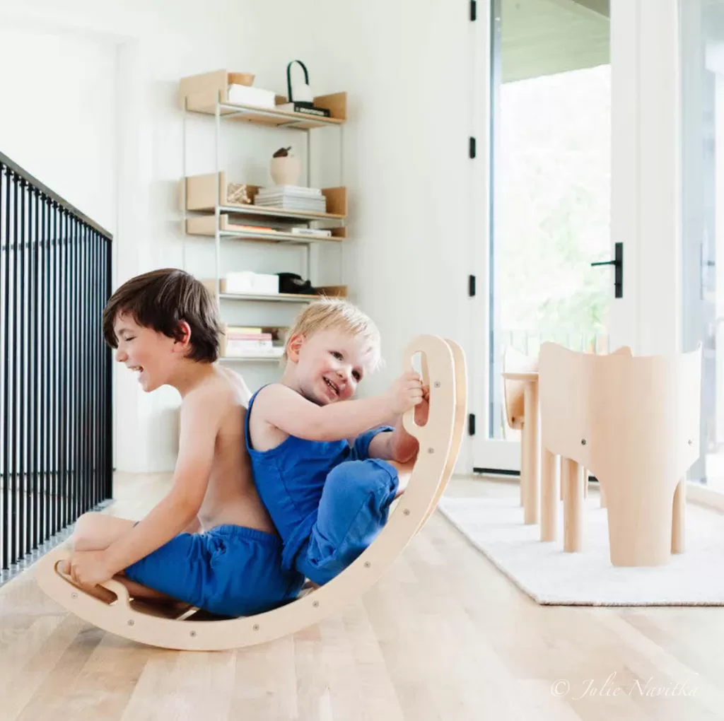 Image of two young children playing on a rocking wooden arch from All Circles. Eco-child's play is beneficial for kids and the environment.