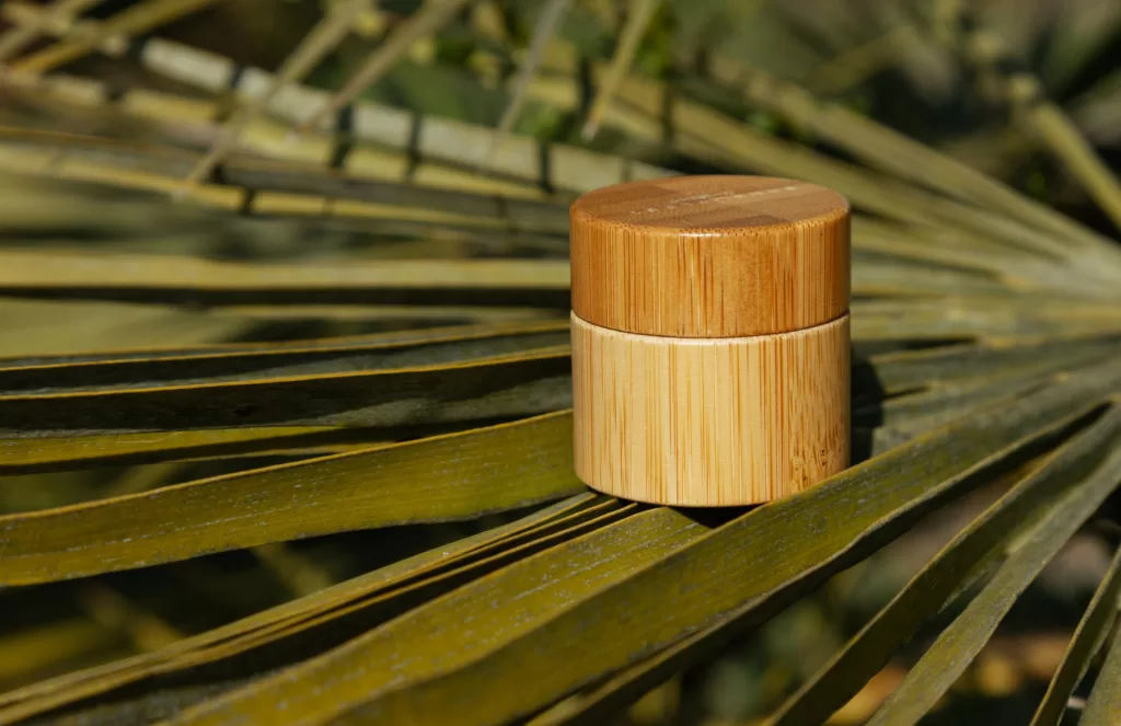Image of a small bamboo container sitting on a palm frond. Bamboo is a more eco-friendly way to package beauty products than plastic.