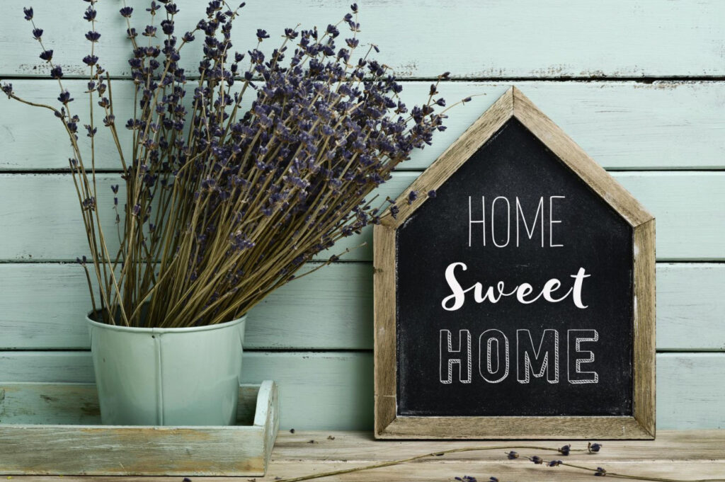 Image of a vase of dried lavender next to a house shaped chalk sign that says "home sweet home"