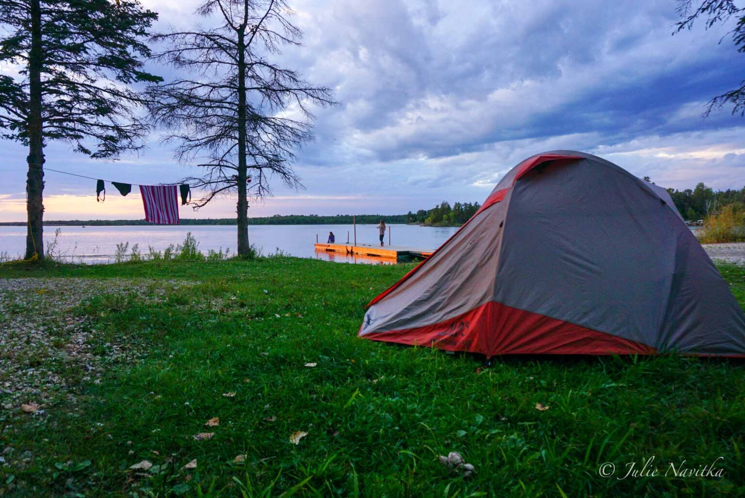 Image of a tent at dusk set up on a patch of grass in front of a lake. Recreating sustainably should be a priority if you love the outdoors.