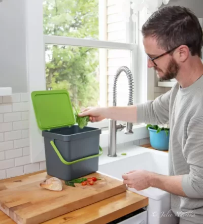 Image of the home compost bin from Terra Cycle on a countertop with a person putting food scraps inside.