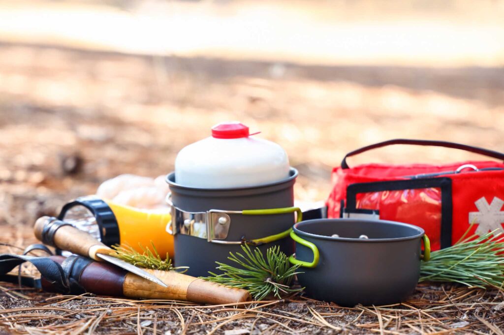 Image of camping gear including first aid kit, camp pot and fuel, flashlight and knife.