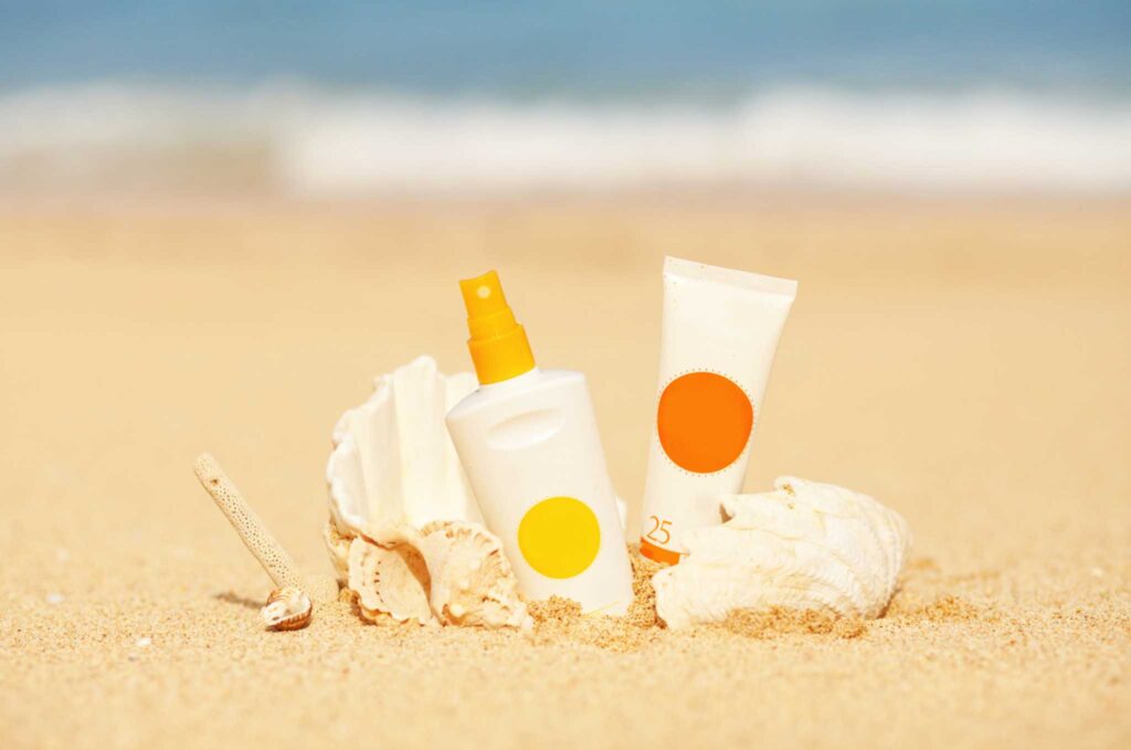 Image of two generic sunscreen bottles sitting in the sand with seashells. Eco-friendly sunscreen is important to protect our aquatic ecosystems.
