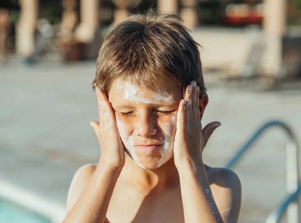 Image of a young child rubbing sunscreen onto their face. Reapply eco-friendly sunscreen often to protect from uva and uvb rays.