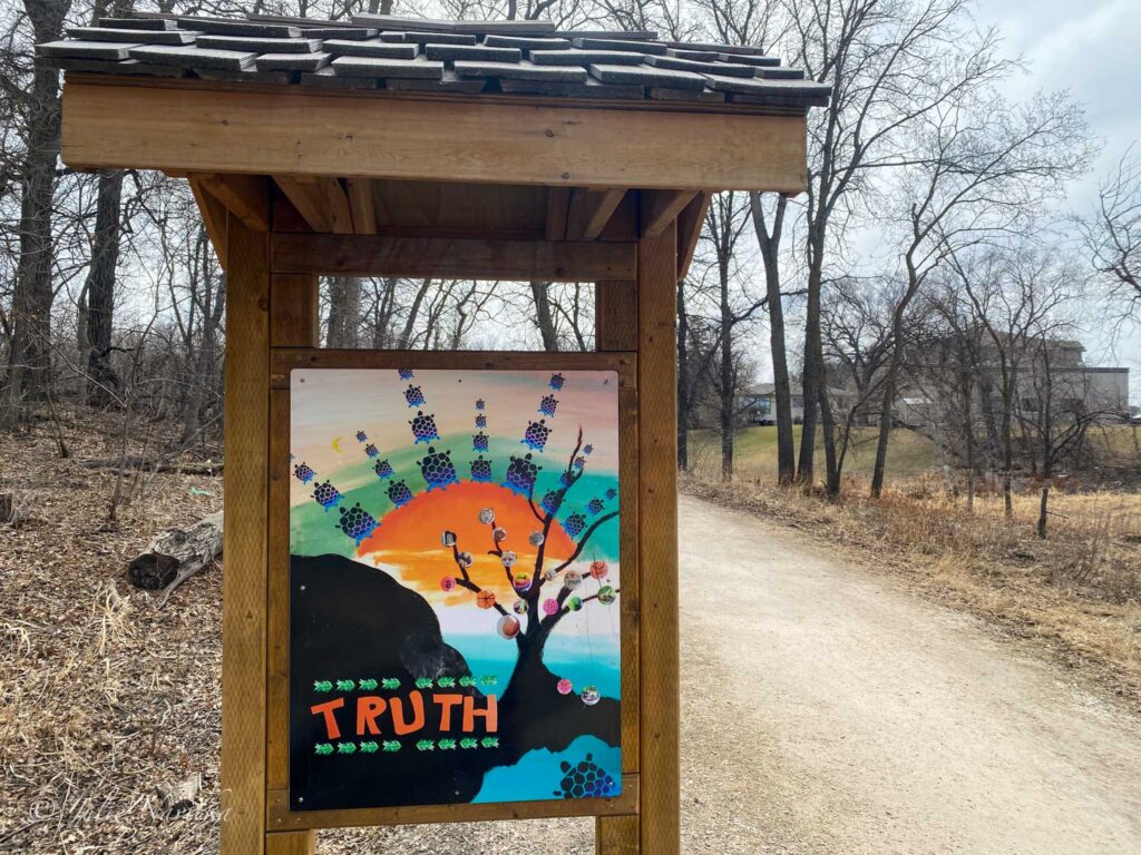 Image of a covered  placard showcasing a piece of art beside a gravel trail in a sustainable community park.