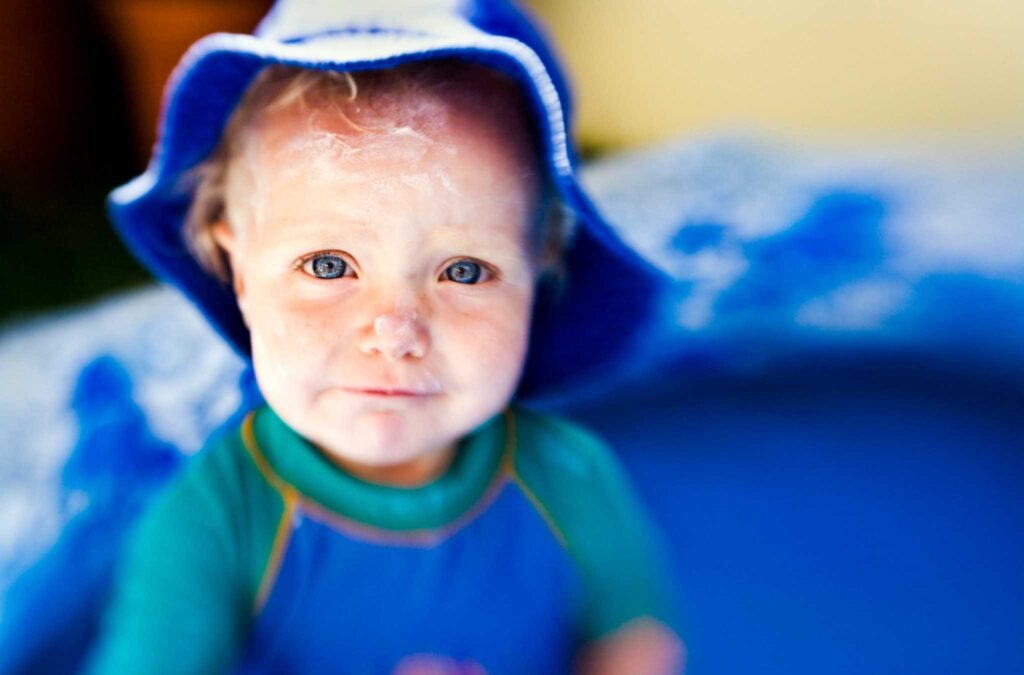 Image of small child wearing a hat with sunscreen slathered on their face. Eco-friendly sunscreen for kids should protect from uva and uvb rays and be water resistant.