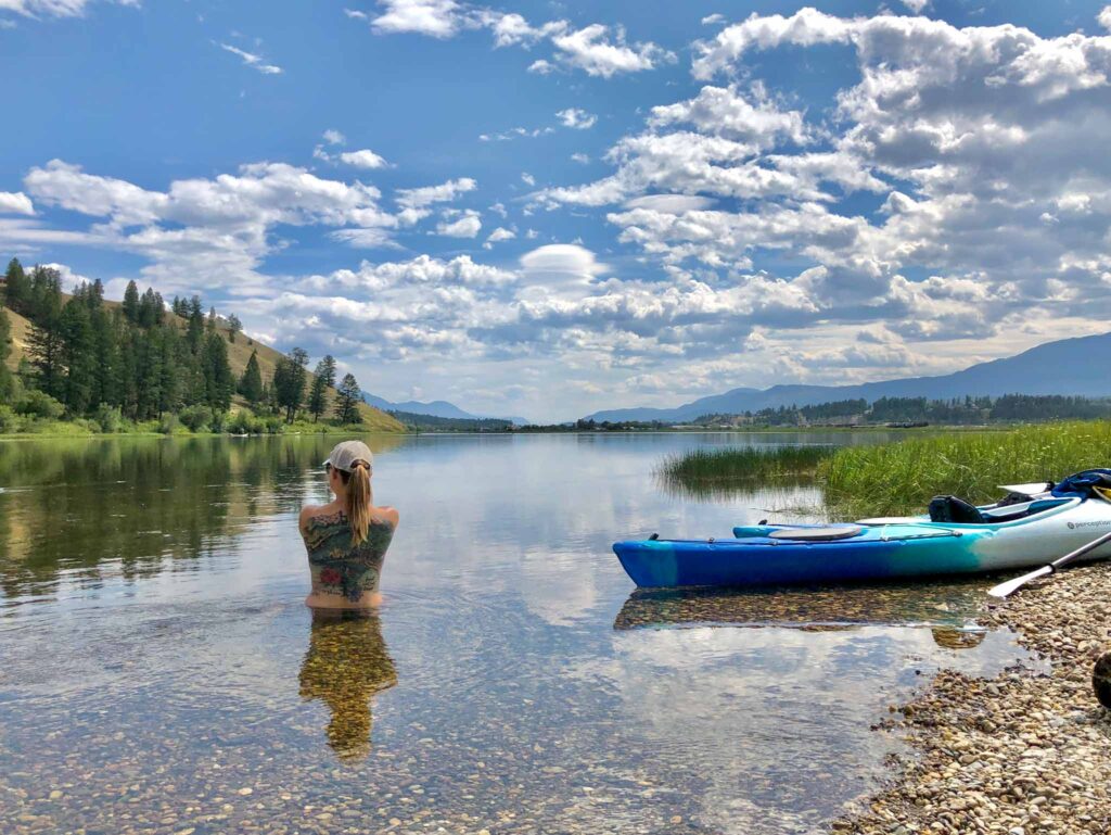 Image of a kayaker sitting in the shallow waters of a lake next to the shore and their kayak. The eco-friendly sunscreen we choose should have broad spectrum protection and natural ingredients.