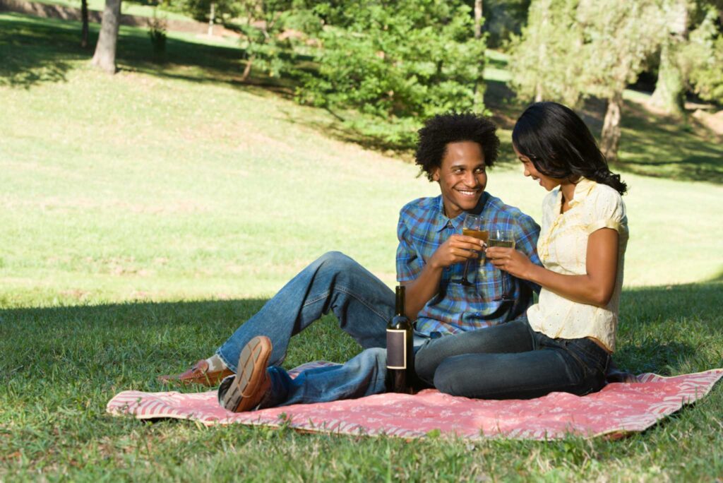 Image of a couple picnicking in a park under the shade of a tree. Seeking shade and covering up are the safest way to protect ourselves from UV rays.