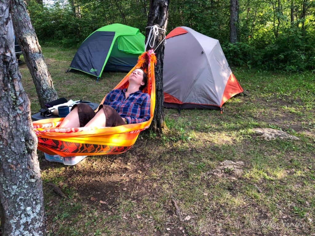 Image of a camper relaxing in a hammock with tents in background. You can rest easy knowing you have done your best to make your camping trip eco-friendly and sustainable.