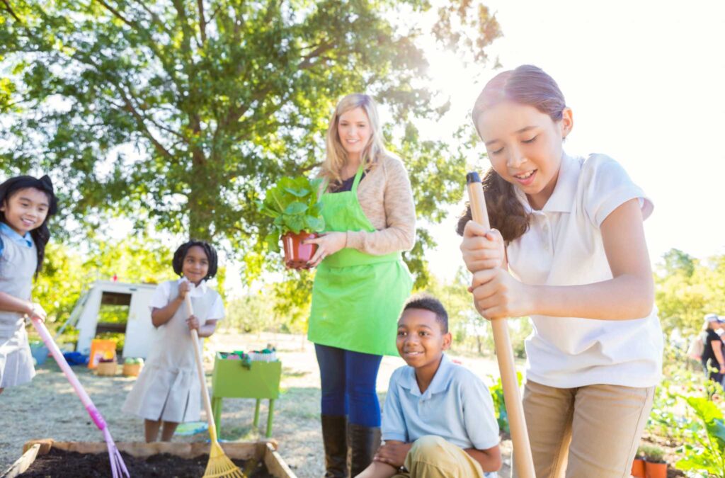 Image of an adult helping kids plant and maintain a garden. A school garden can lead to a more sustainable school.