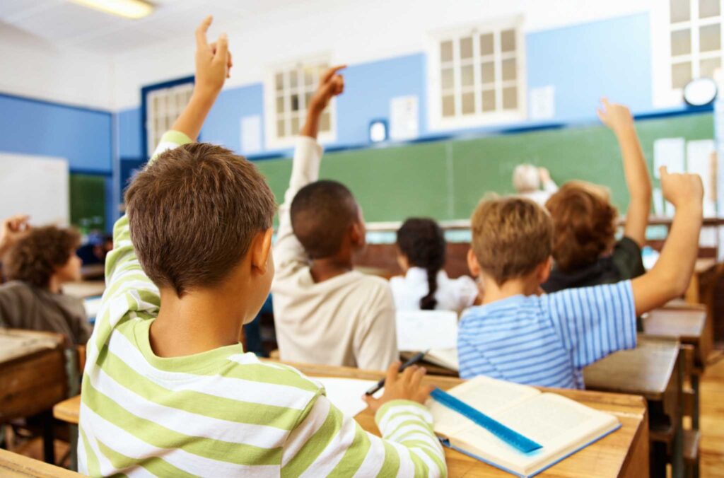 Image from the back of a classroom with students raising their hands. Kids have really creative ideas about how to make the classroom more eco-friendly.