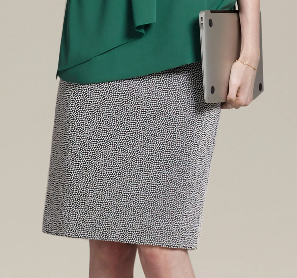 Image of the M.M. LaFleur Noho Skirt worn by a model carrying a laptop. Some sustainable work clothing brands create a circular loop by re-selling used items returned by customers at discounted prices.
