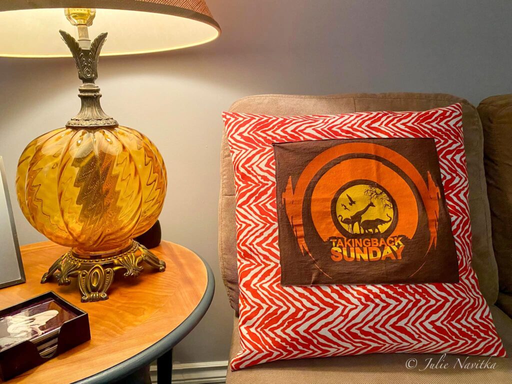 Image of a throw pillow made with an old tshirt and thrifted material sitting beside a vintage lamp.
